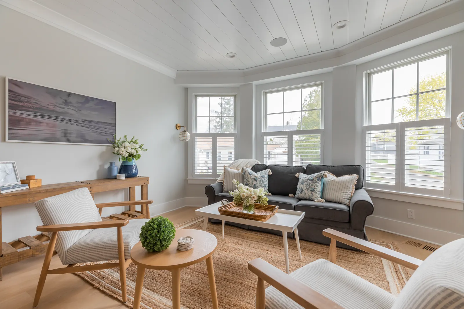 A bright coastal living room with white plantation shutters on a bay of windows